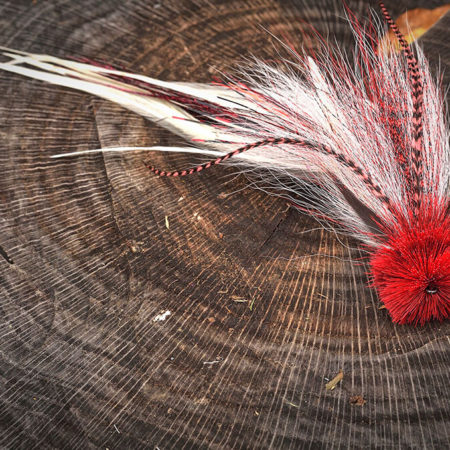 Classic pike fly fishing lure with red and white feathers, displayed on a tree stump.