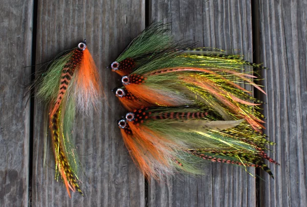 Set of Urban Fly Co. lures with vibrant orange, green, and feathered designs for fly fishing, displayed on a wooden surface.