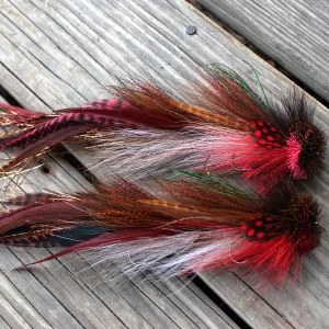 Pair of Urban Fly Co. lures with red and brown feathers, designed for fly fishing, arranged on a wooden surface.