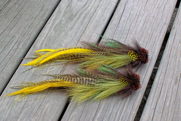 Urban Fly Co. Smallmouth Double Buford fishing lures with a vibrant mix of yellow, brown, and green feathers, displayed on a wooden deck.