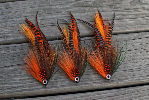 Urban Fly Co. Sucker Single Minnow fishing lures in vibrant orange and black, displayed on a wooden deck.