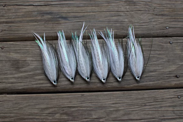 Urban Fly Co. collection of white Bendback fishing lures with realistic eye details, displayed on a wooden surface, highlighting their sleek and streamlined design.