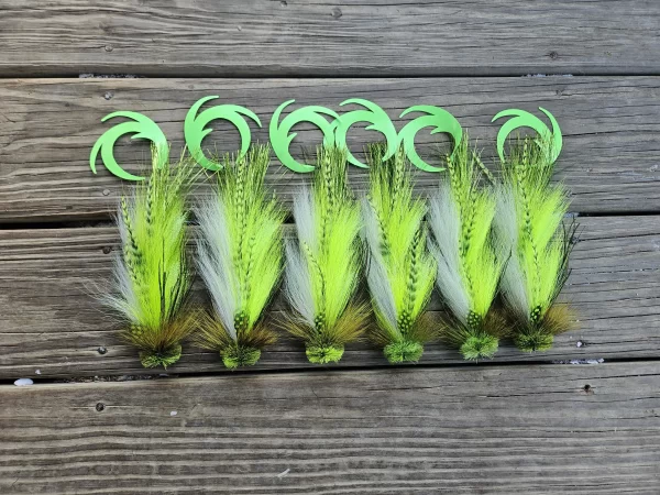 A row of fly fishing lures from Urban Fly Co. featuring vibrant feathers in shades of green and white, with green tails, arranged on a wooden surface.