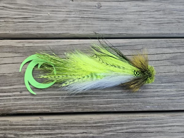 A fly fishing lure from Urban Fly Co. featuring vibrant feathers in shades of green and white, with a green tail, placed on a wooden surface.