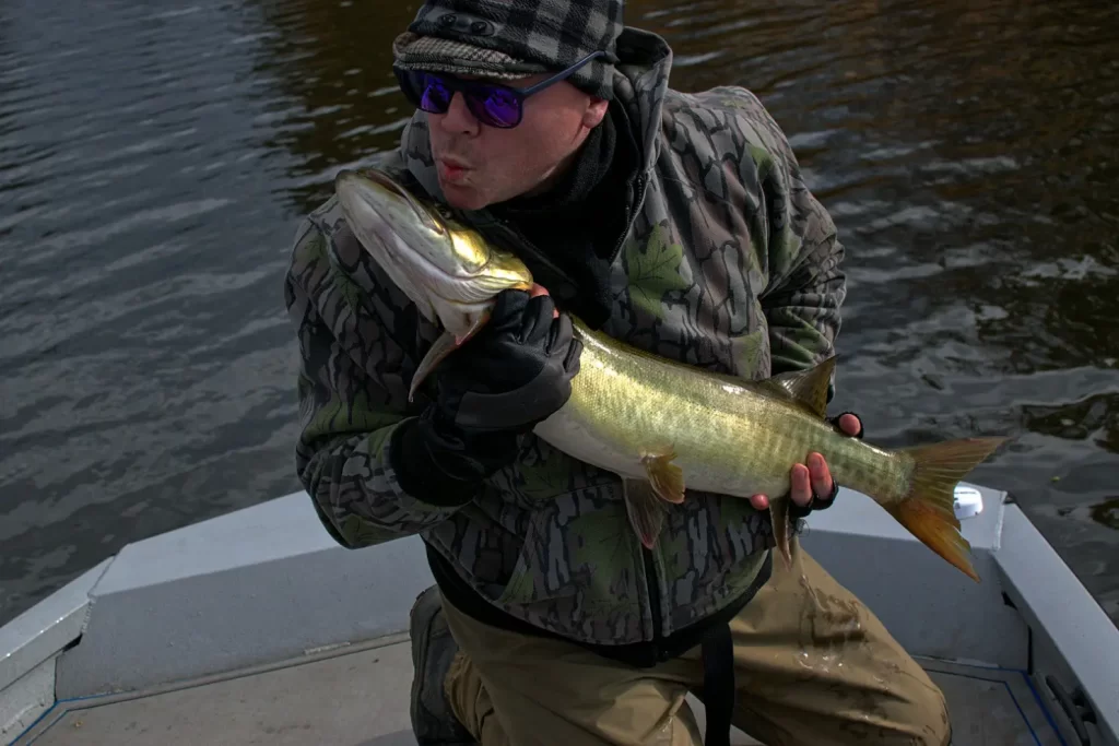 A fisherman in a boat faux kissing a fish he has caught