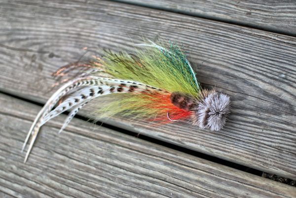 Colorful fly fishing lure with green, orange, and white feathers, laid out on a wooden surface.