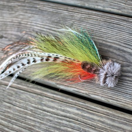 Colorful fly fishing lure with green, orange, and white feathers, laid out on a wooden surface.