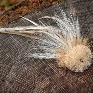 All-white Urban Fly Co. fly fishing lure with feathers, displayed on a tree stump.