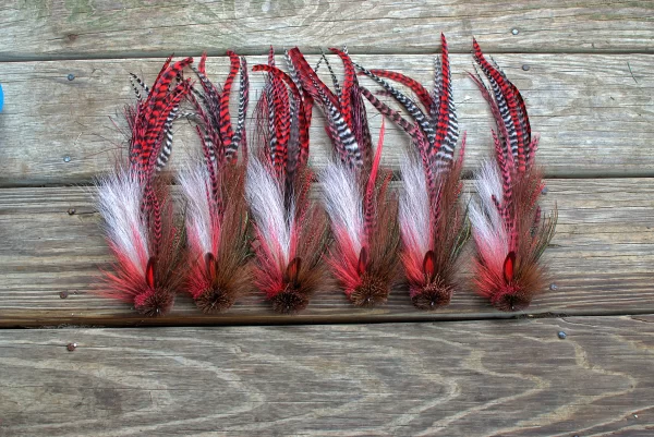 Urban Fly Co. collection of red and brown feathered fishing lures arranged on a wooden surface, showcasing intricate feather patterns and textures.