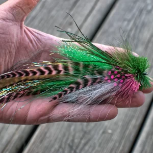 Hand holding a vibrant green and pink Urban Fly Co. lure with striped feathers and a bushy head, showcasing its detailed craftsmanship.