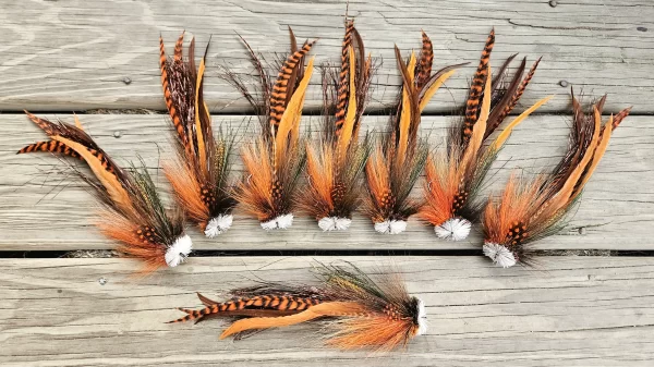 Urban Fly Co. collection of orange and brown feathered fishing lures displayed on a wooden surface, highlighting detailed feather patterns and textures.