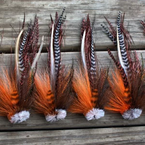 Urban Fly Co. collection of orange and brown single Buford fishing lures displayed on a wooden surface, showcasing detailed feather patterns and textures.